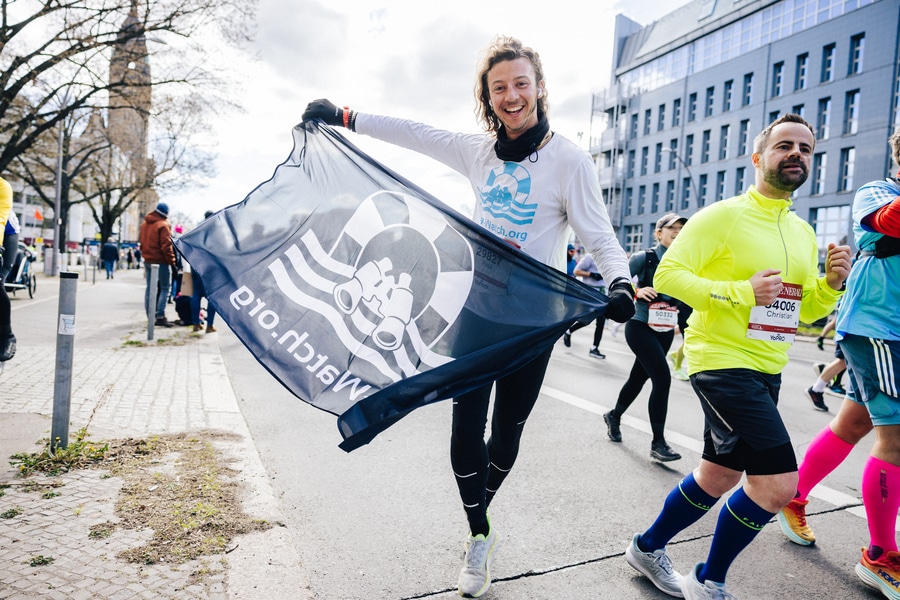 Ein Läufer schwenkt bei seinem Spendenlauf auf dem Halbmarathon eine Sea-Watch-Flagge.